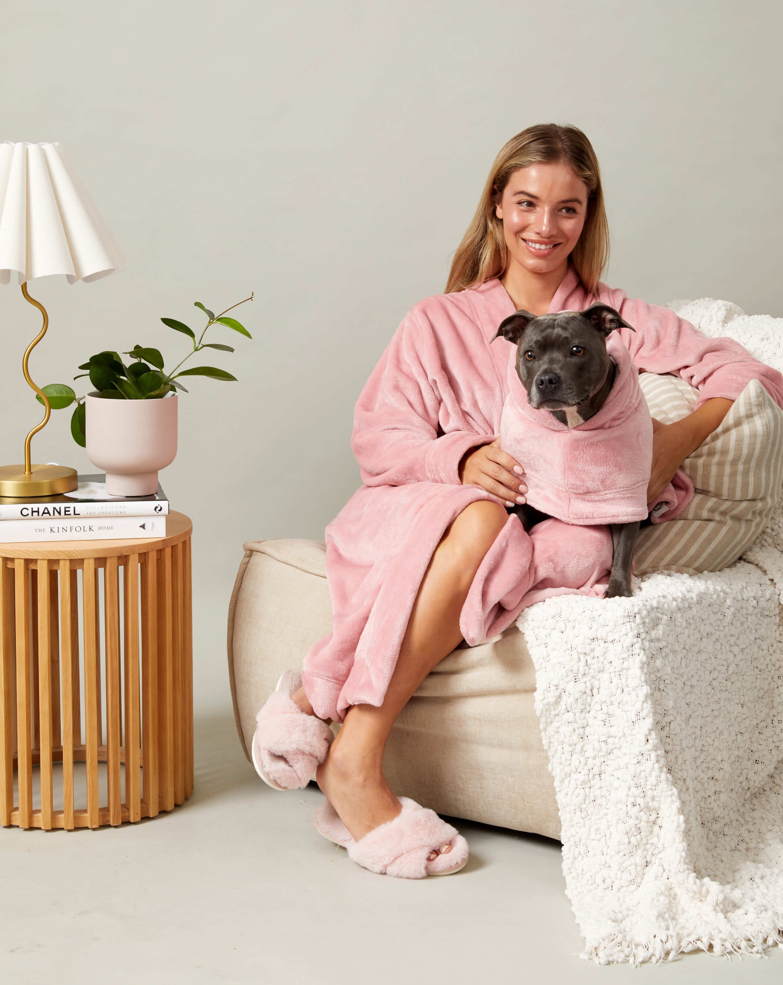 A women cuddling her dog on the couch wearing match your dog pink fluffy robes.